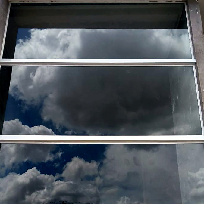 Janela de vidro com perfis de alumínio refletindo o céu