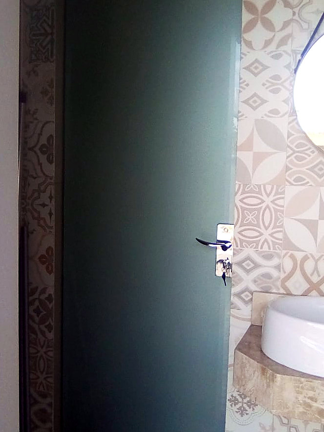 Porta de vidro jateado verde em banheiro com revestimento estampado
